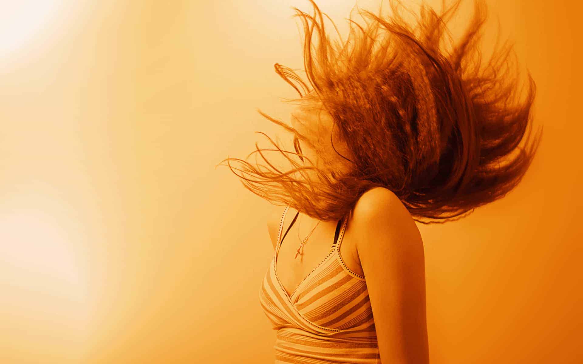 mujer con cabello volando en fondo anaranjado