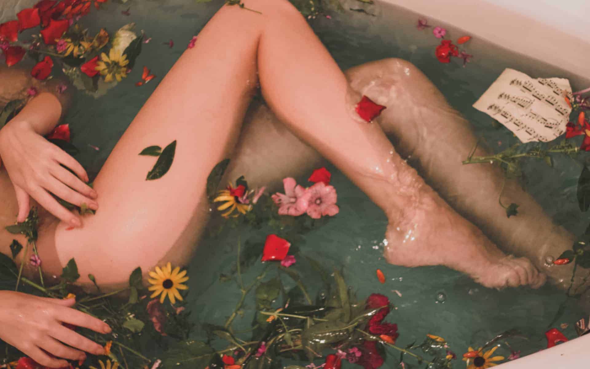 Chica en tina de baño con agua y flores, solo se ven sus piernas.
