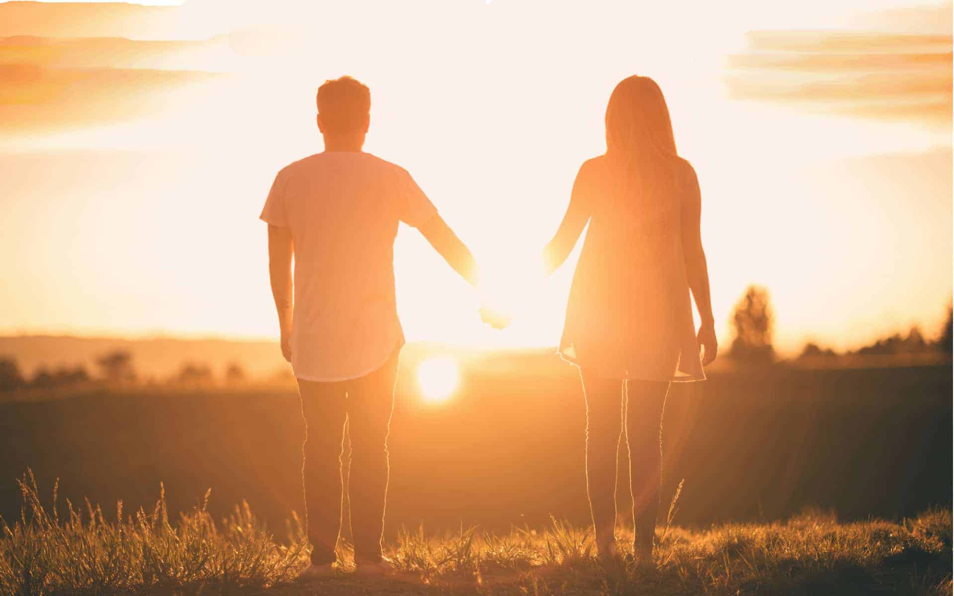 Una pareja se toma de la mano mientras ve la puesta del sol.