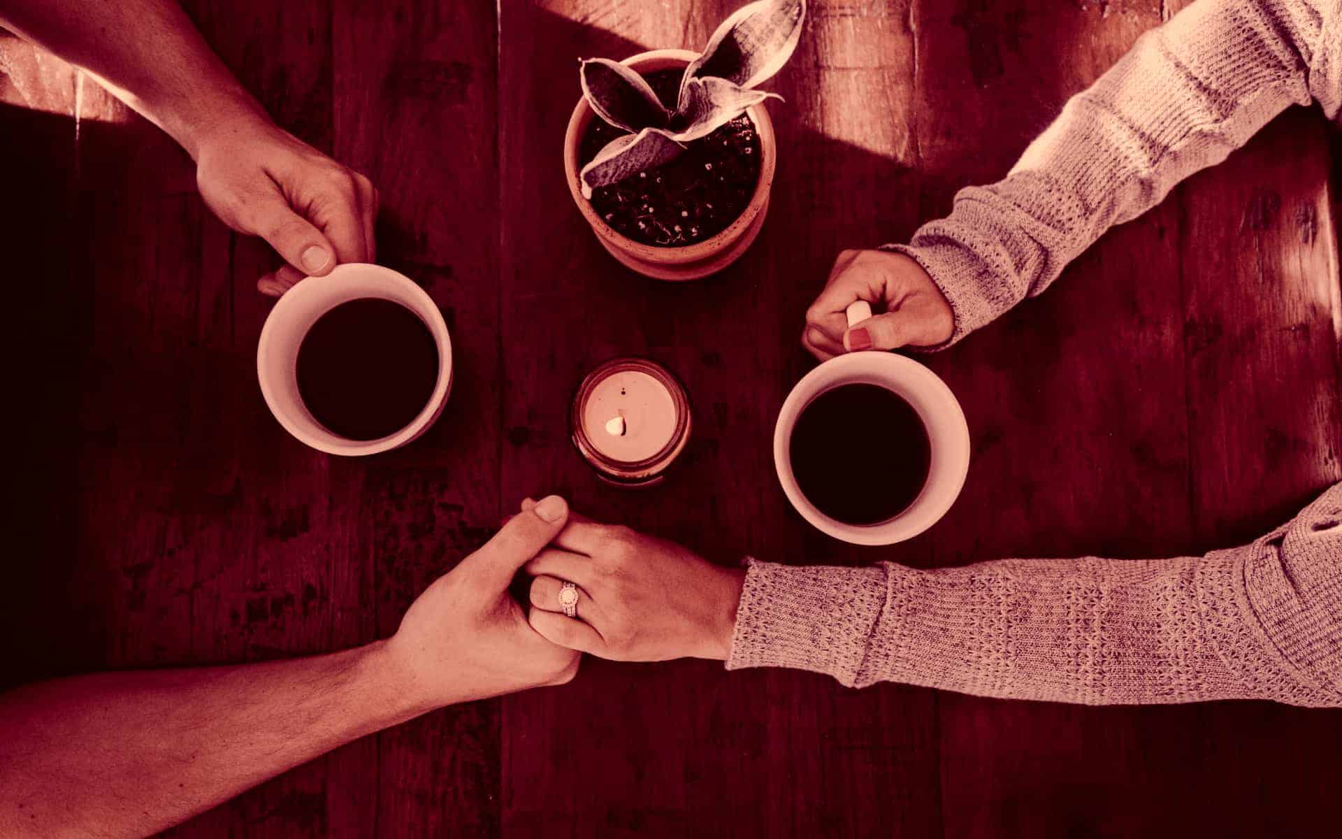 Se ven los brazos de dos personas que se dan la mano, mientras toman un café.
