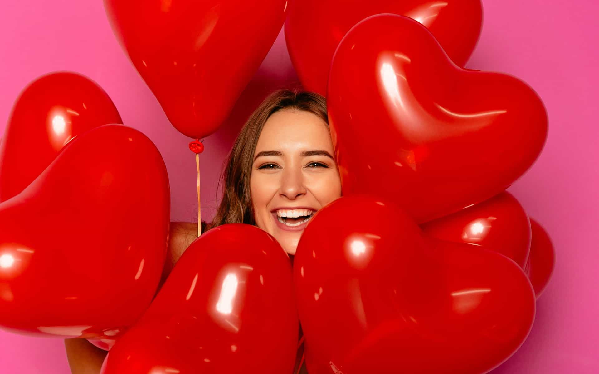 Día de San Valentín. Chica sonriente mirando la cámara, mirando un montón de globos.