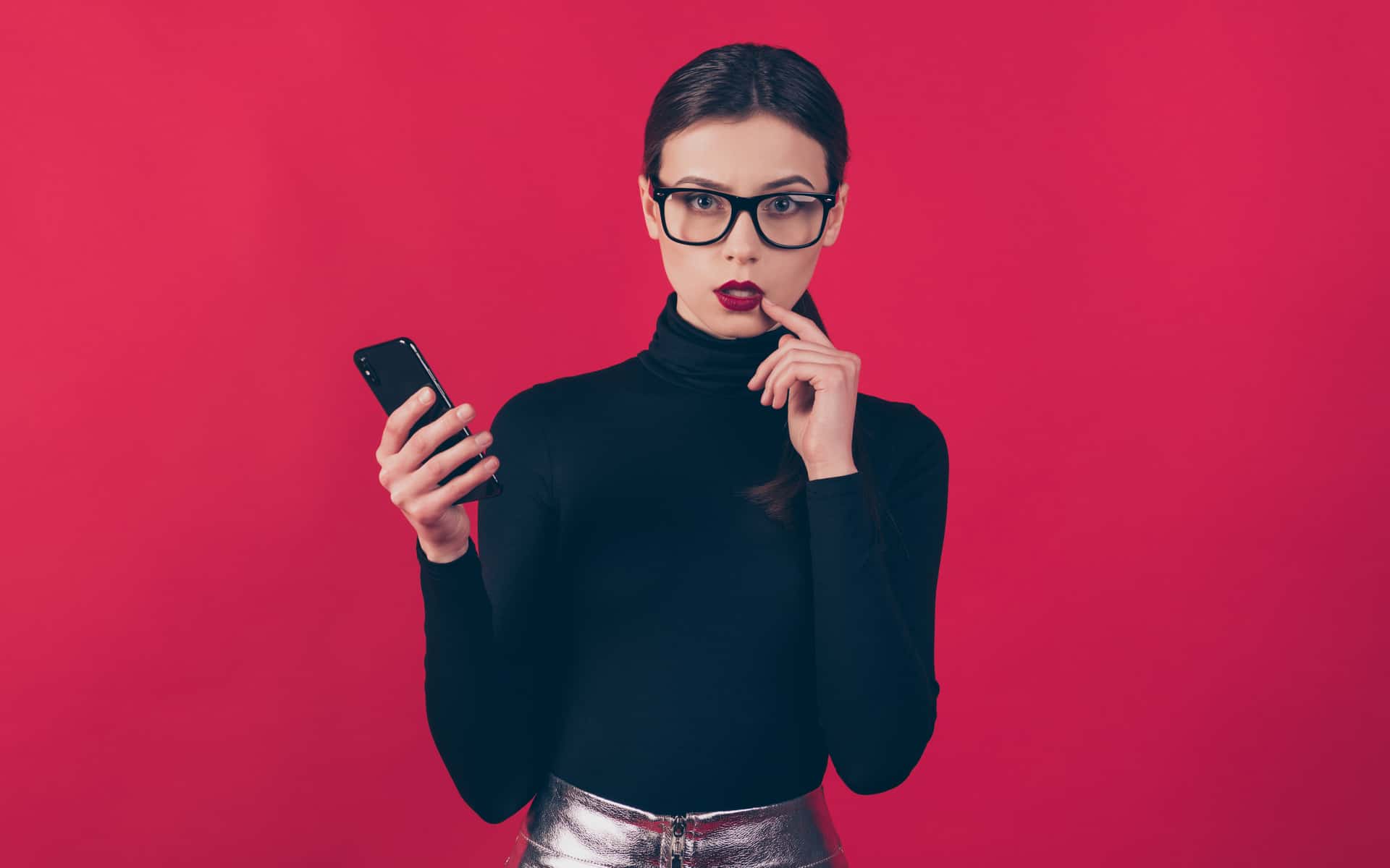 mujer joven con celular en la mano y expresión pensativa en fondo rojo