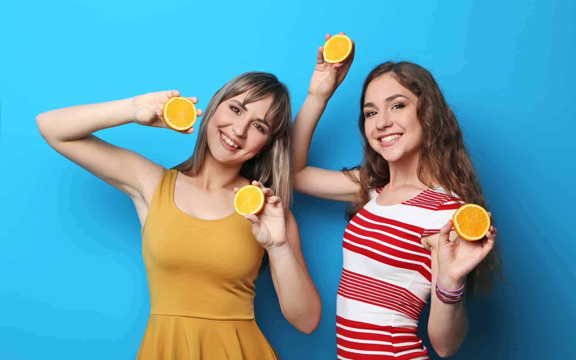dos mujeres jóvenes con naranjas en las manos en fondo azul