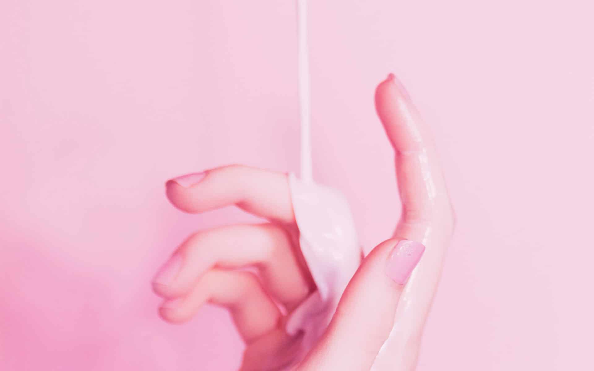 mano con liquido blanco en fondo rosa