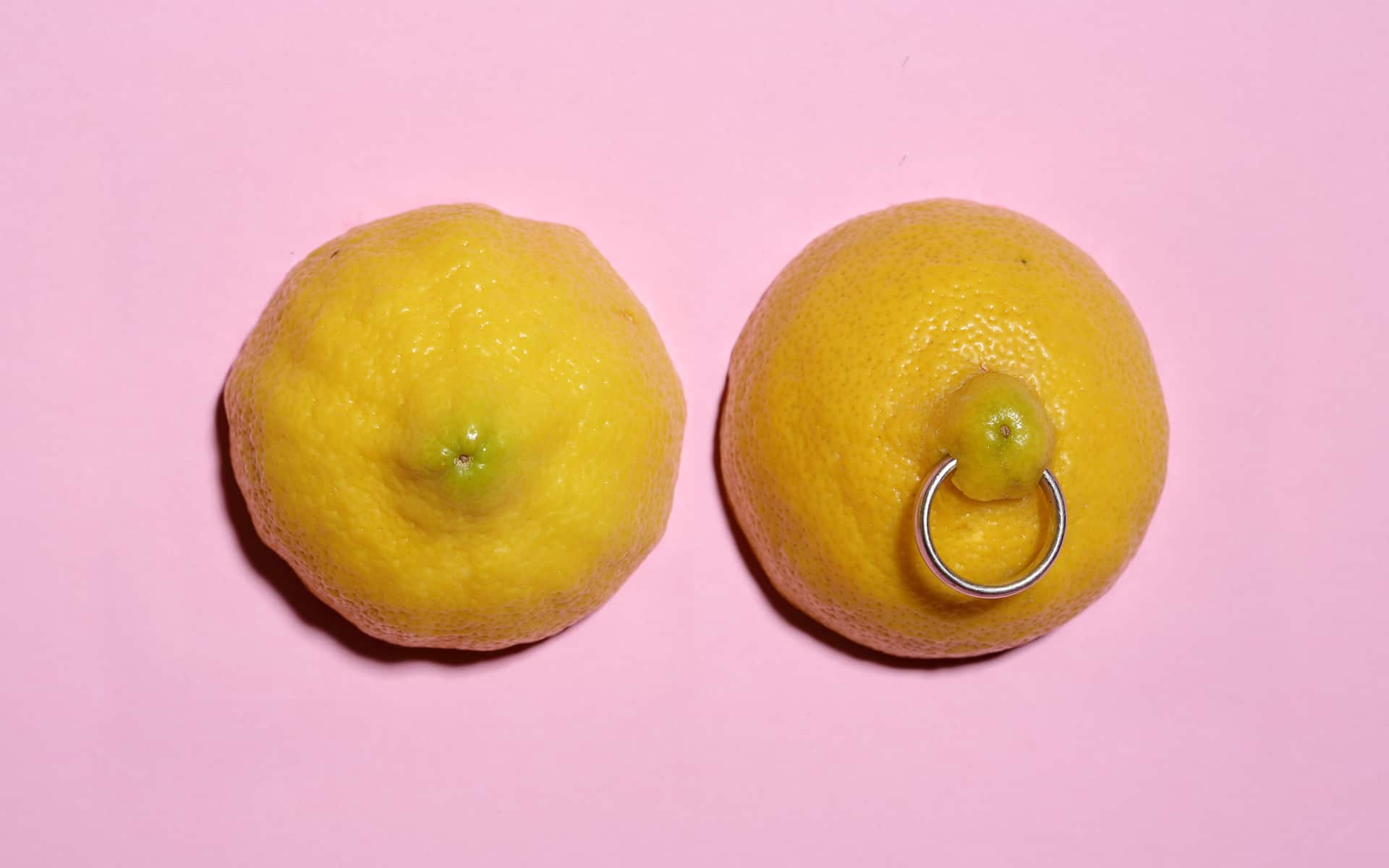 dos mitades de limón con perforación de anillo sobre fondo rosa pastel