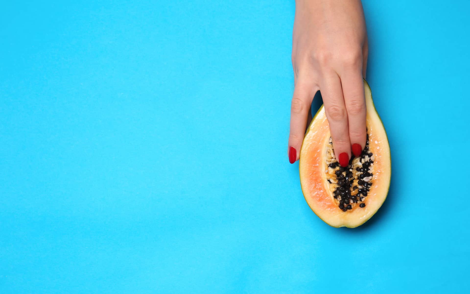 Mano femenina y la mitad de papaya fresca sobre fondo de color. Concepto erótico