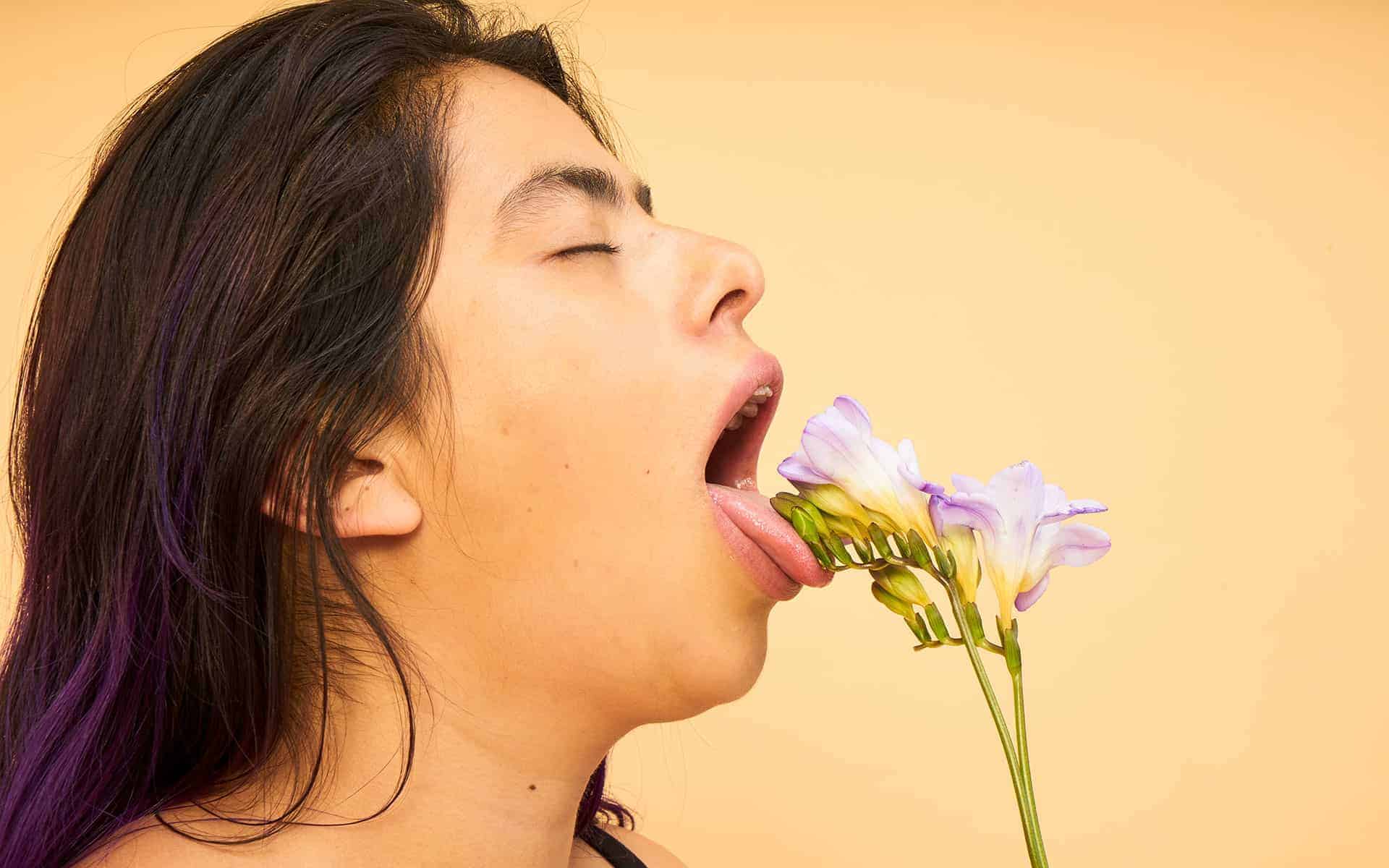 close up mujer con fondo color piel con flor en boca