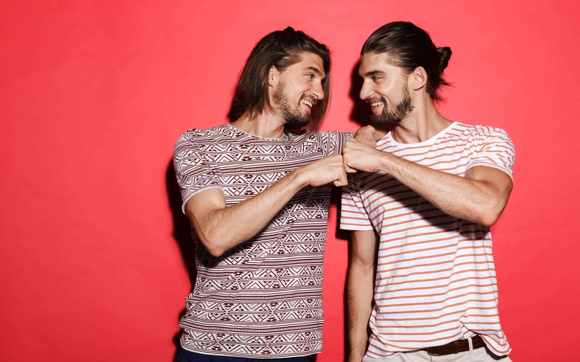 Retrato de dos hermanos gemelos sonrientes parados aislados sobre fondo rojo, dando un chocalas