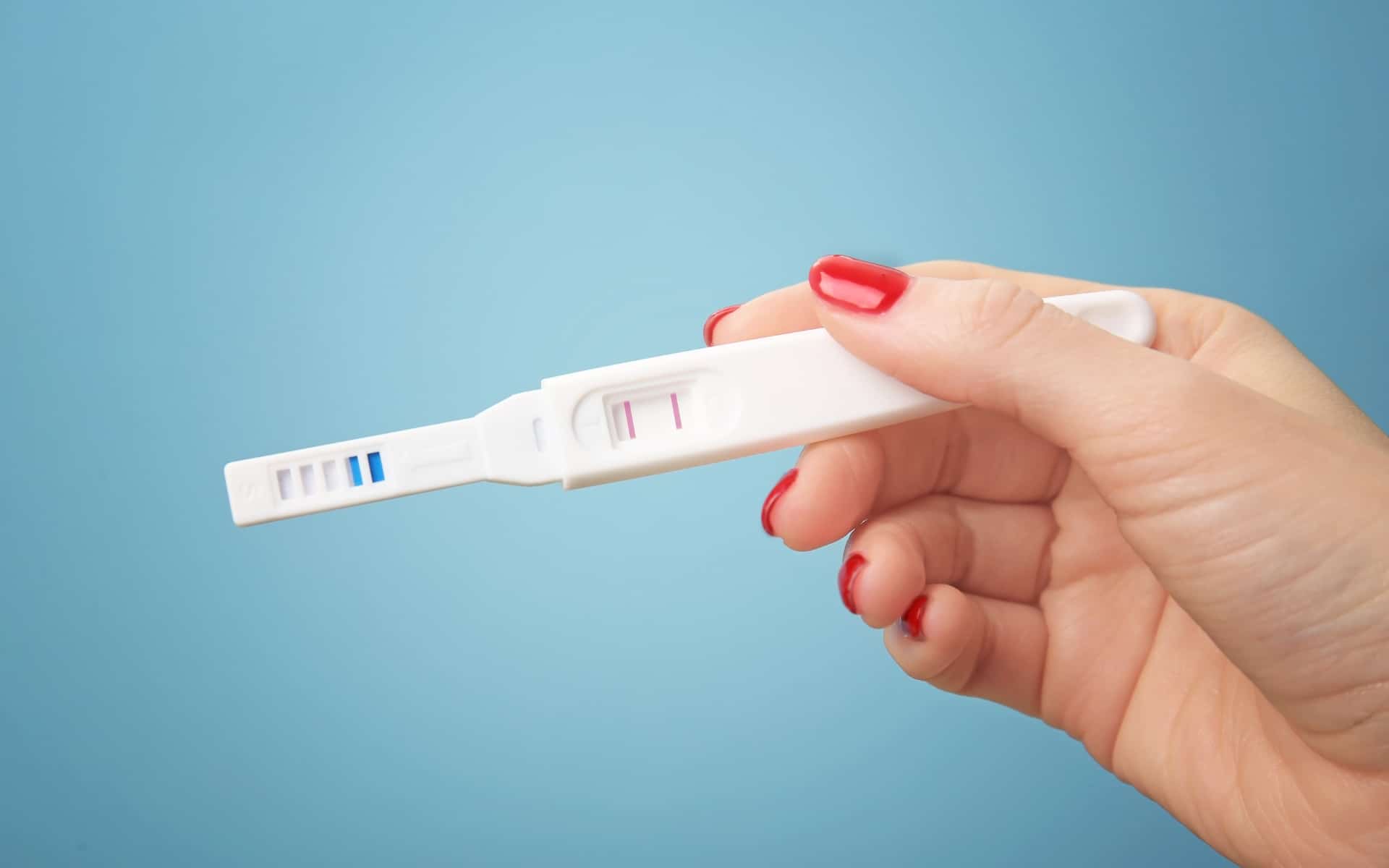 prueba de embarazo en mano en fondo azul